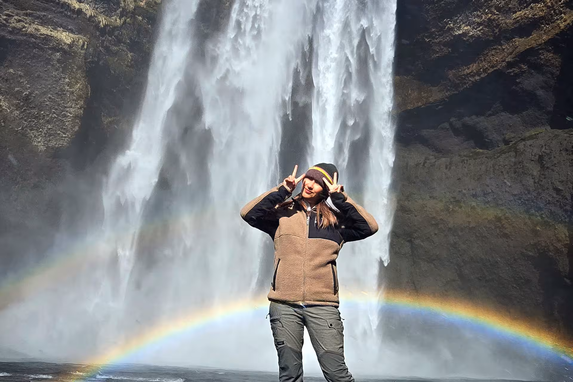 A woman staning in front of a waterfall and a rainbow