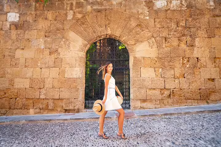 Woman in a white dress poses in front of a historic stone archway during a private photoshoot in Rhodes.