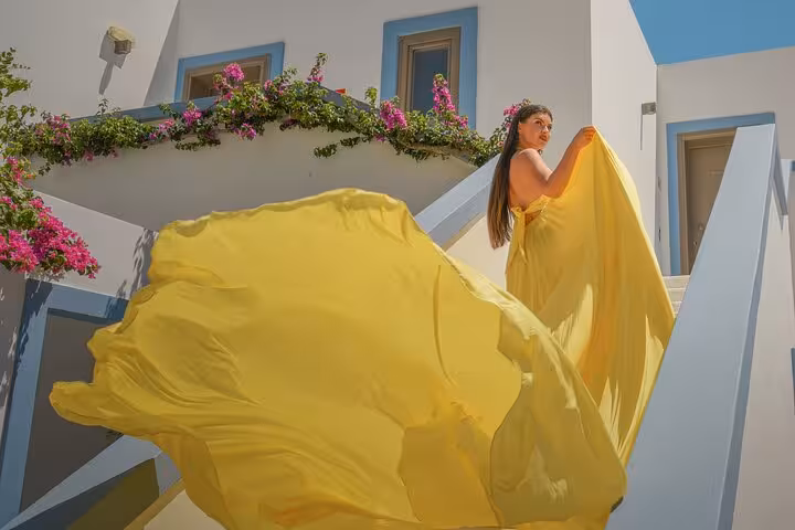Woman in flowing yellow dress poses on stairs with vibrant flowers during Heraklion flying dress photoshoot experience.