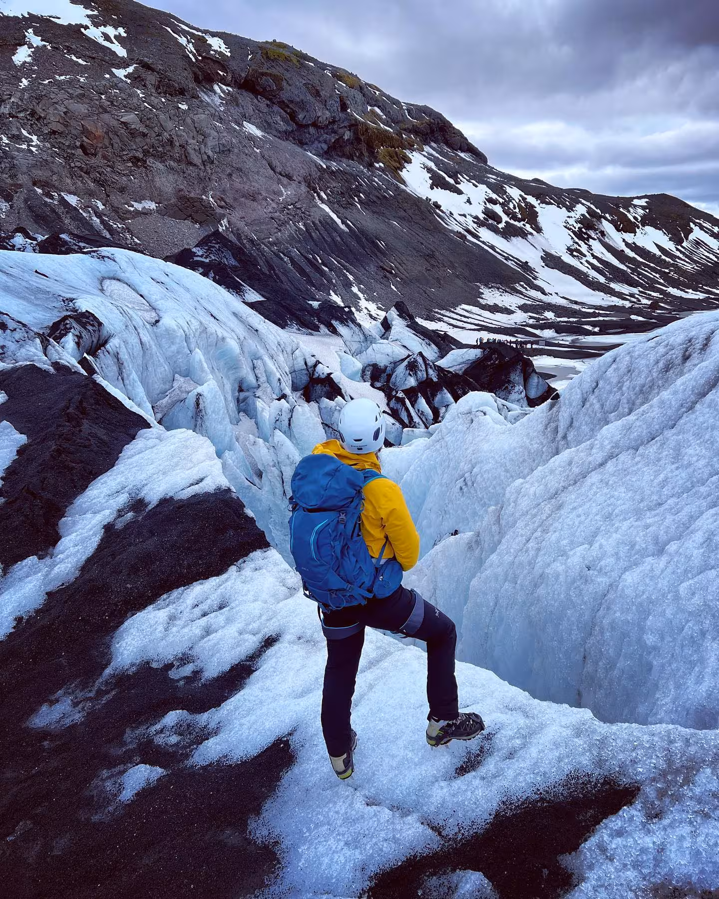 Woman in yellow jacket and helmet explores icy glacier terrain in Iceland on a women's 7-day adventure tour.
