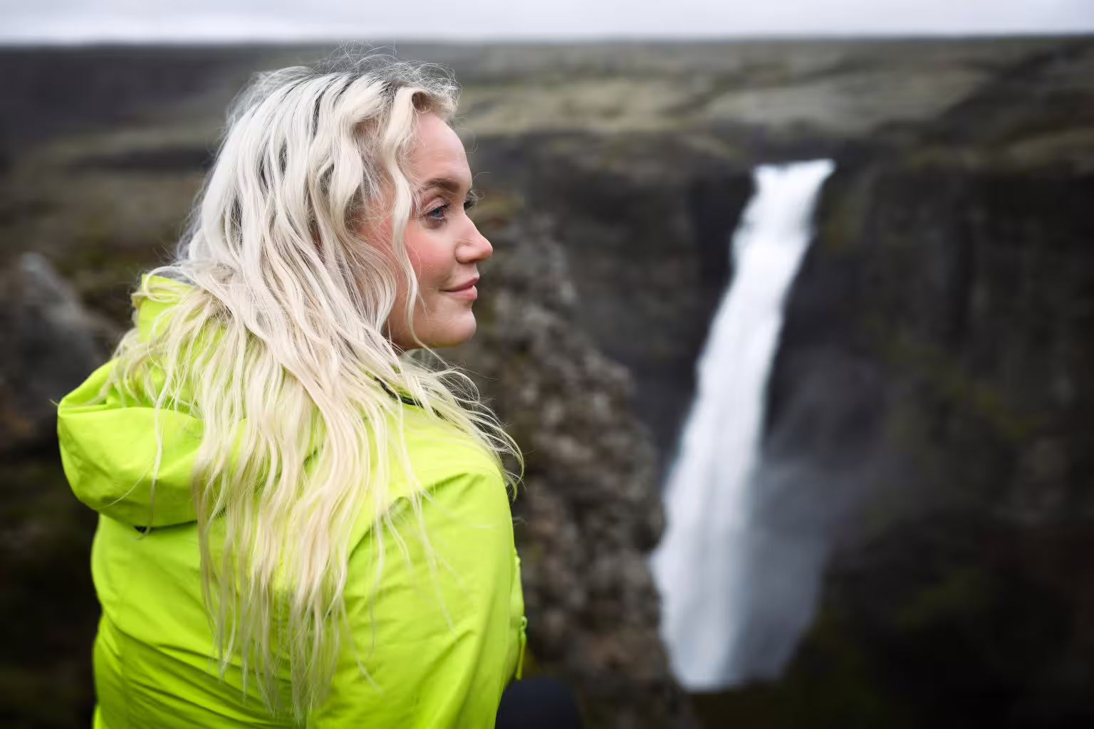 A woman in a bright yellow jacket gazes at a stunning Iceland South Coast waterfall during a Viking Valley summer adventure tour