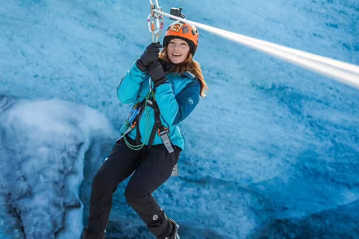 Smiling woman zip-lining on a glacier adventure near Glacier Lagoon Iceland wearing safety helmet and harness