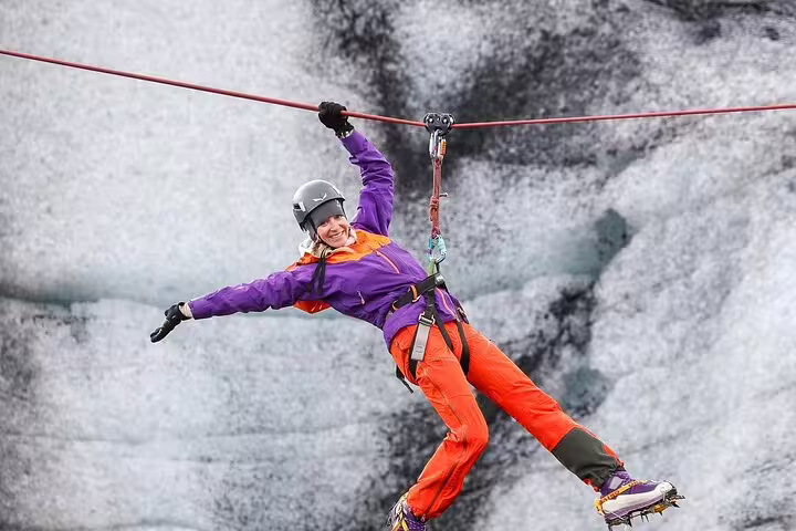 Woman zip-lining in colorful gear over Iceland glacier ice wall on thrilling Glacier Lagoon adventure tour