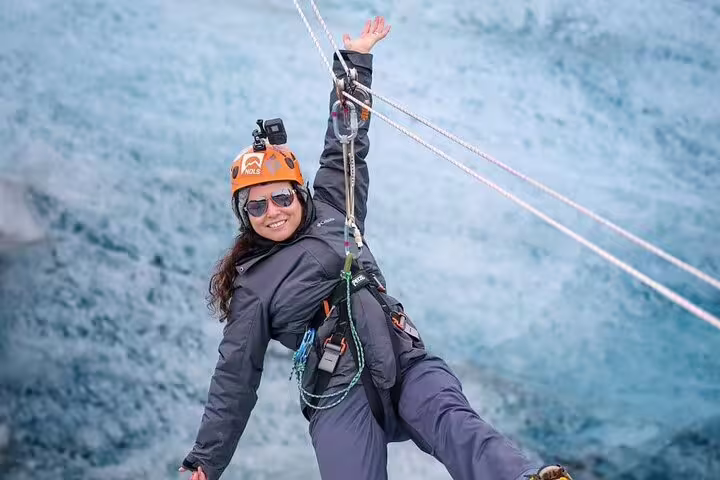 Smiling woman in orange helmet and harness zip-lining over Iceland glacier lagoon adventure tour