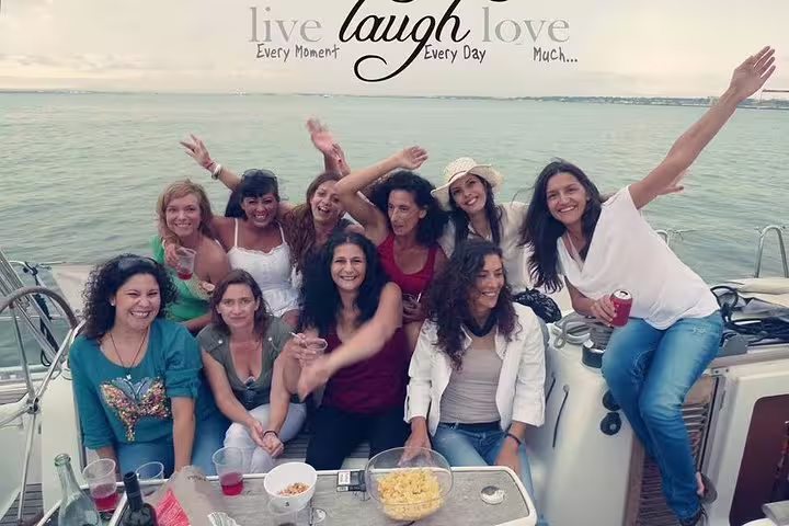 Happy group of women celebrating on a sailboat during a Lisbon private sailing tour with drinks and laughter.