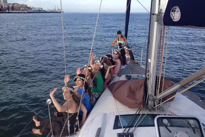 Smiling group of women with flower crowns wave from a yacht deck on a private Lisbon sailing tour.