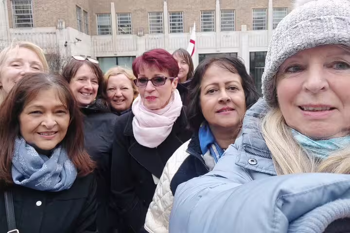 Group of women smiling together on a London self-guided walking tour outdoors near a brick building