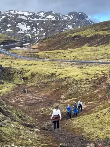 Women hike through the lush, mossy terrain of the Icelandic Highlands with snow-capped mountains in the background.