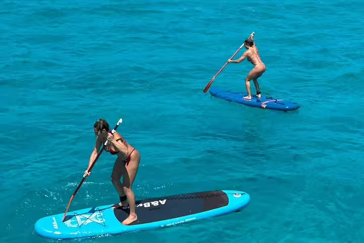 Two women paddleboarding on clear turquoise waters during a sailing trip in Ibiza and Formentera, enjoying the sun.