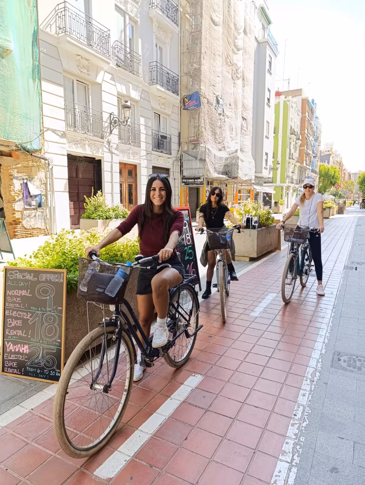 Women riding Dutch-style Omafiets city bikes on a sunny urban street, step-through frames and front baskets