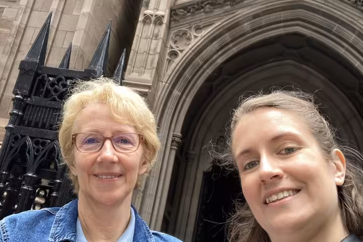 Two women smiling in selfie outside historic stone Gothic arch building entrance in Manhattan NYC