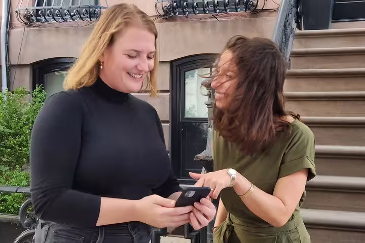 Two women smiling and looking at a smartphone during a walking tour in NYC