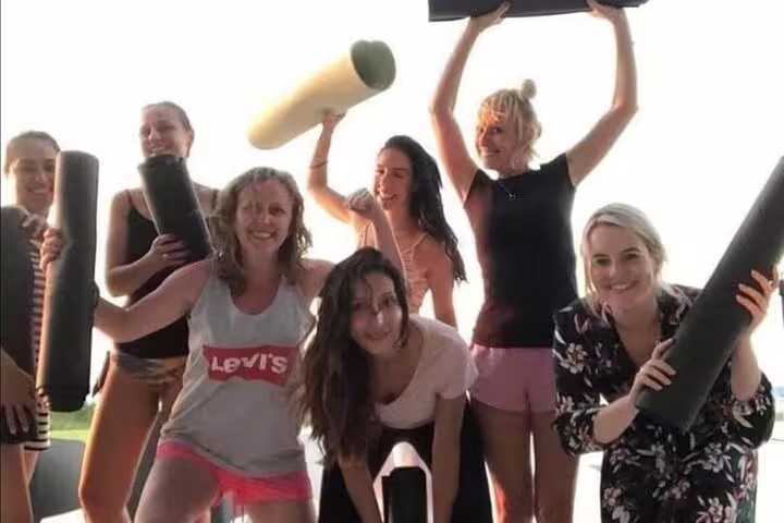 Group of women enjoying vibrant yoga session in Kos, holding mats and smiling, highlighting community and wellness.