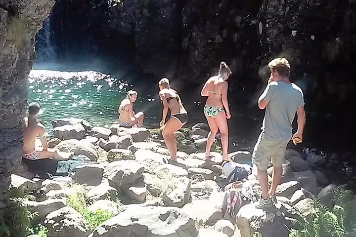 Hikers pause to admire the scenic waterfall and clear pool on the Wood Levada Levada trail, surrounded by rocky terrain.