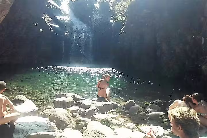 Group of tourists relax by a crystal-clear pool beneath a cascading waterfall on the Wood Levada Levada adventure.