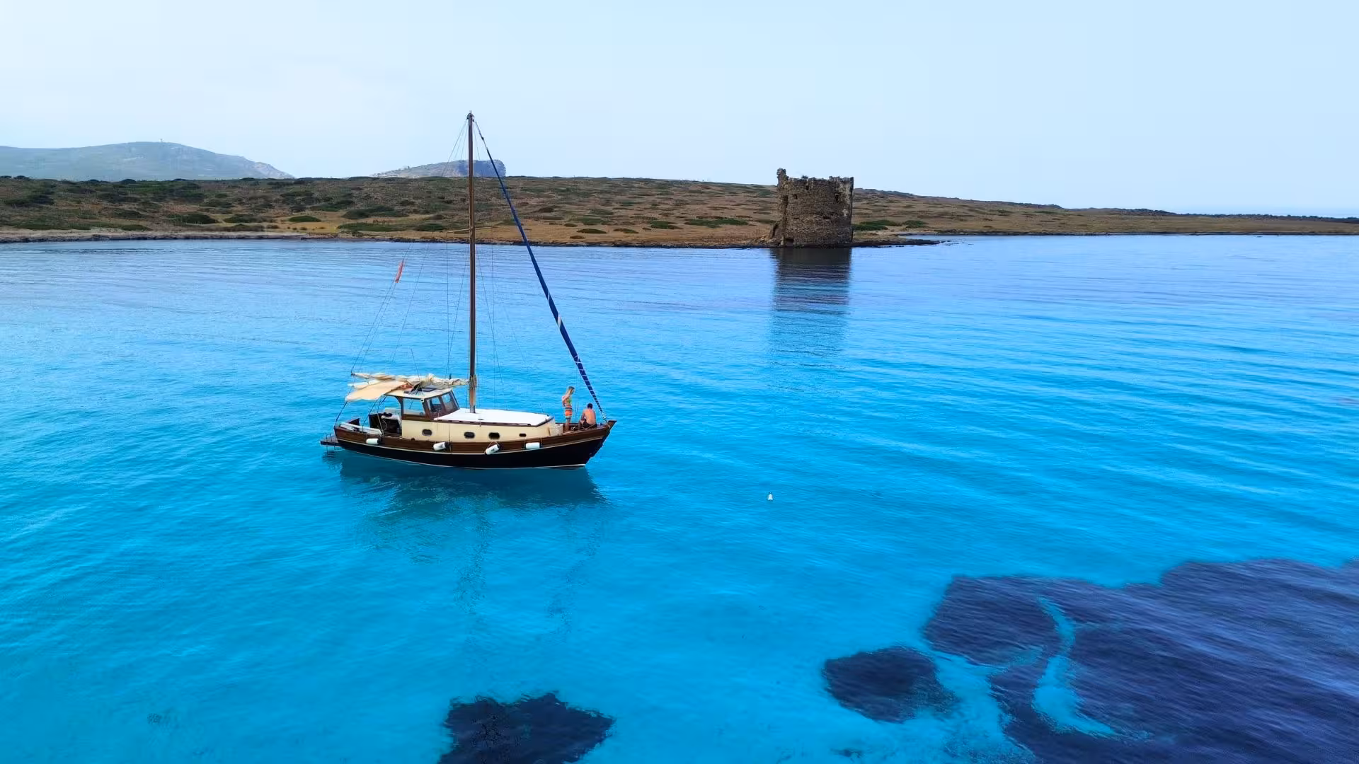 Wooden boat sailing near Asinara Island's clear blue waters and ancient tower, part of Stintino tour.