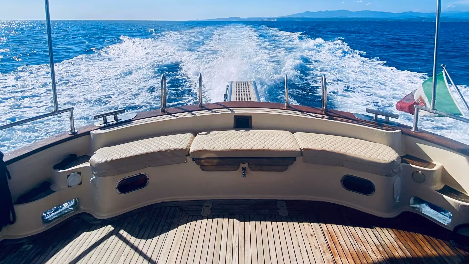 View from a wooden boat on a scenic tour in southern Corsica, featuring sparkling blue waters and distant islands.