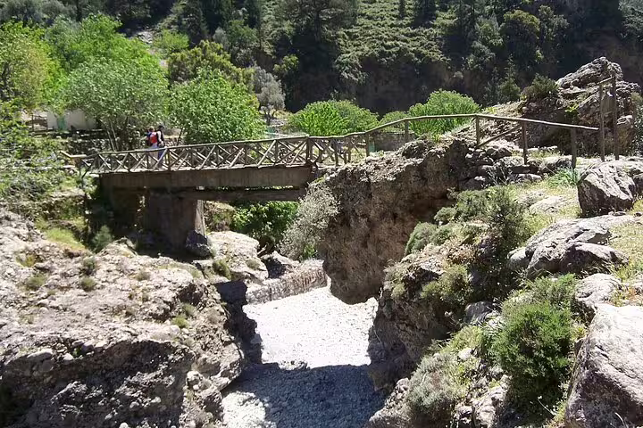 Discover a scenic wooden bridge over a rocky creek amidst lush greenery on the hiking trail in Southwest Crete.