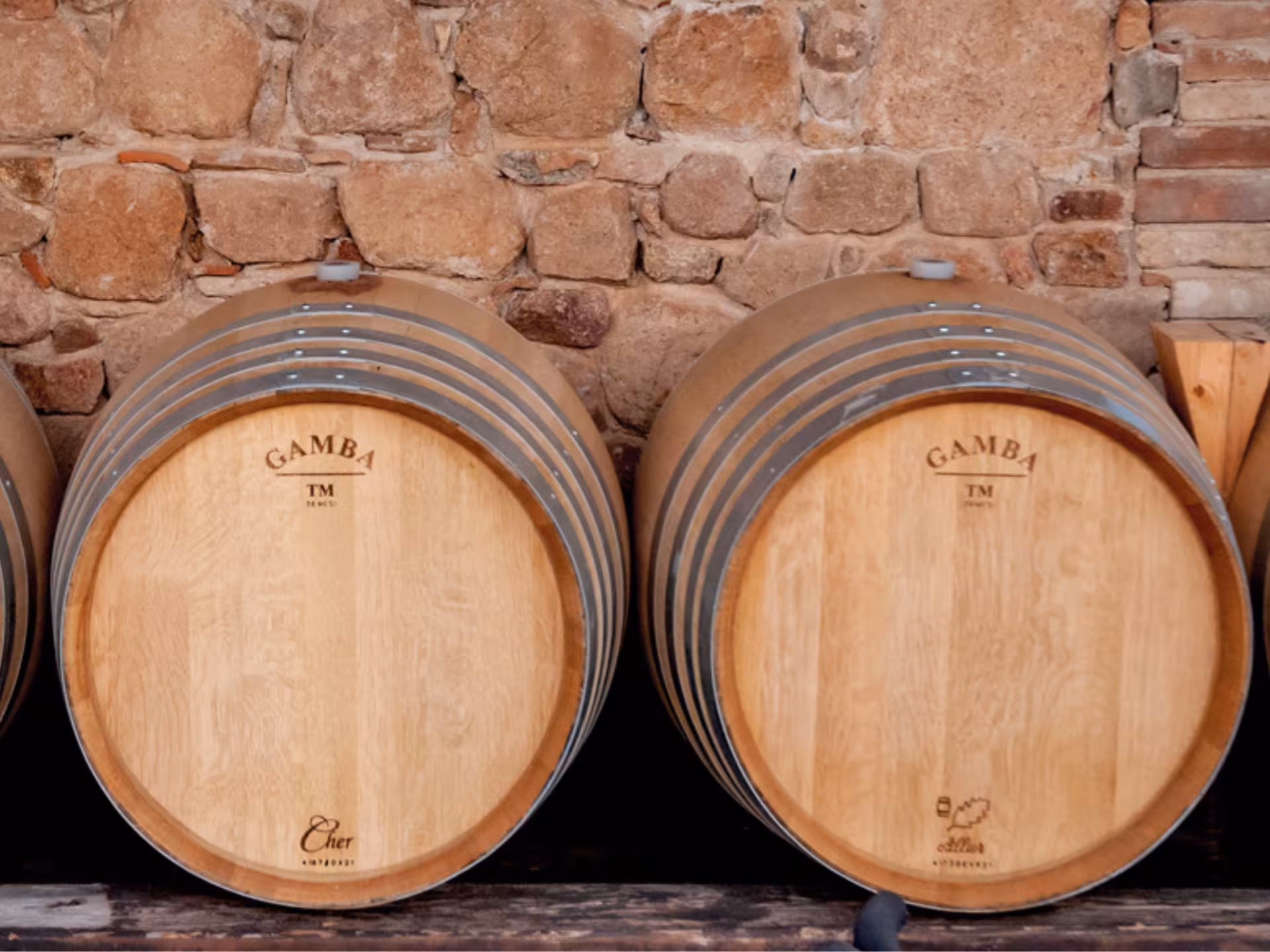 Close-up of wooden wine barrels stacked against a stone wall at a Cagliari countryside winery.