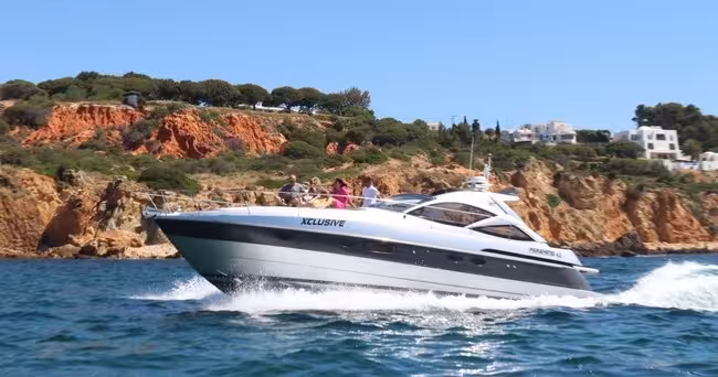 Xclusive Private Luxury Yacht speeding past Algarve cliffs with guests relaxing on deck during a scenic private boat tour