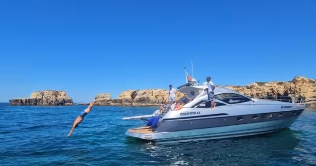 Guest dives into clear Algarve waters from an Xclusive Private Luxury Yacht anchored near dramatic coastal rock formations
