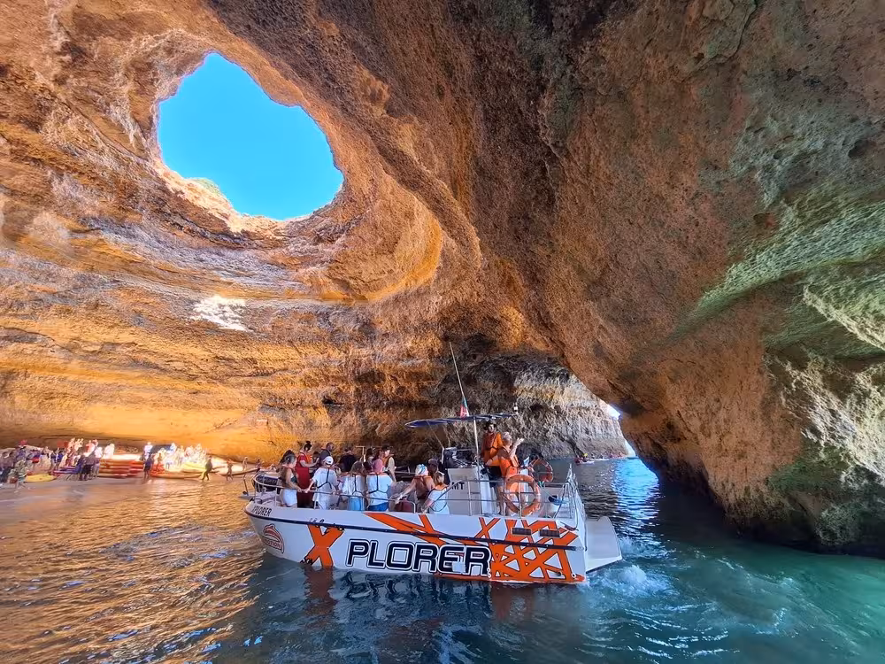 X Plorer caves and dolphins cruise boat entering Benagil sea cave in Algarve, Portugal with tourists and golden cliffs