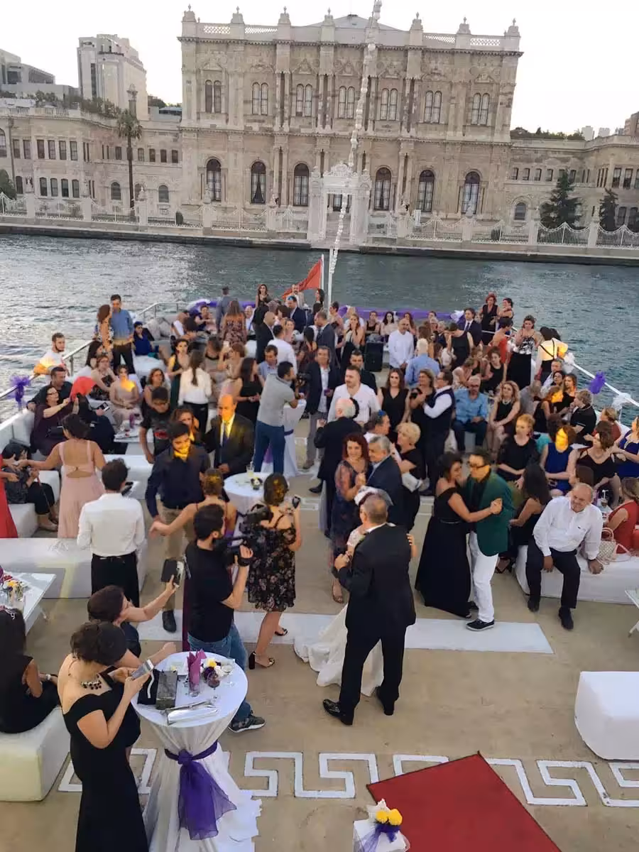 Lively yacht birthday party cruise with dancing guests on deck by Istanbul Bosphorus waterfront palace