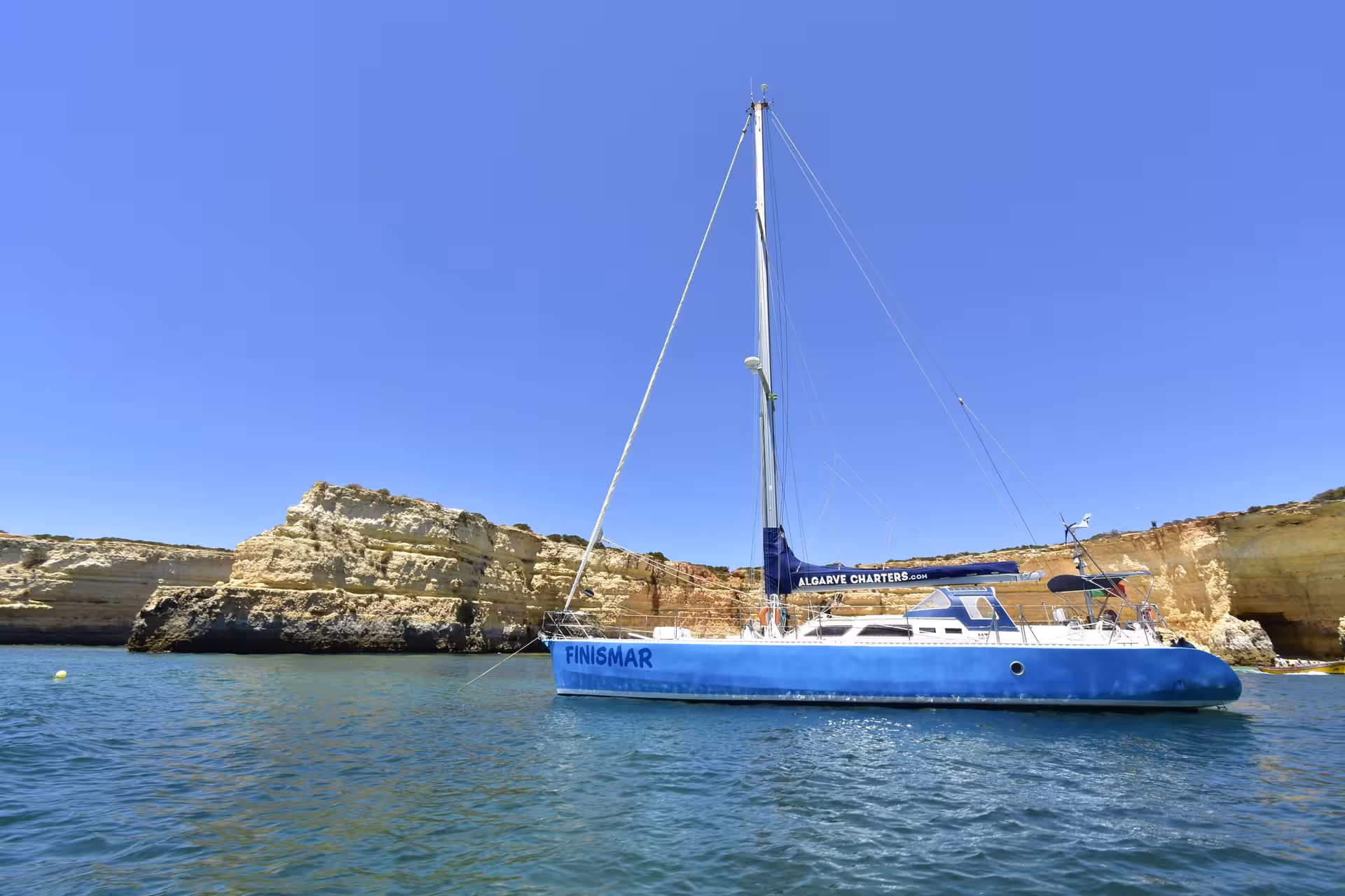 Yacht FINISMAR moored by dramatic Algarve rock formations, ideal for exclusive 2-hour private sailing adventures.