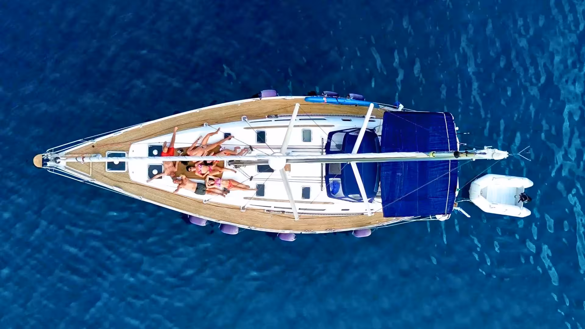 Aerial view of a yacht with sunbathers on deck sailing in the Gulf of Orosei's clear blue waters near Arbatax.