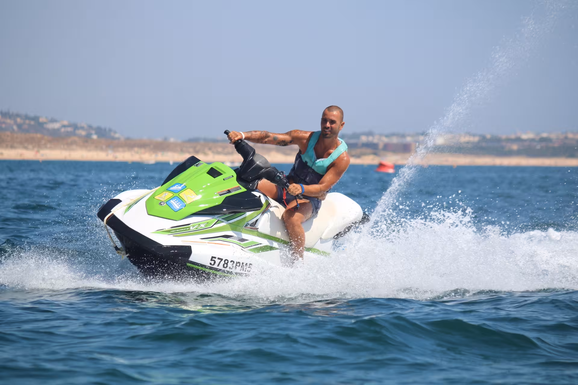 Man in a teal life vest riding a green Yamaha jet ski through choppy coastal waters at speed.