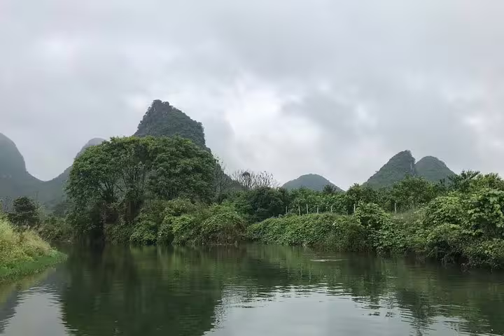 Scenic view of Yangshuo's lush greenery and karst mountains reflected in the calm Li River on a cloudy day.