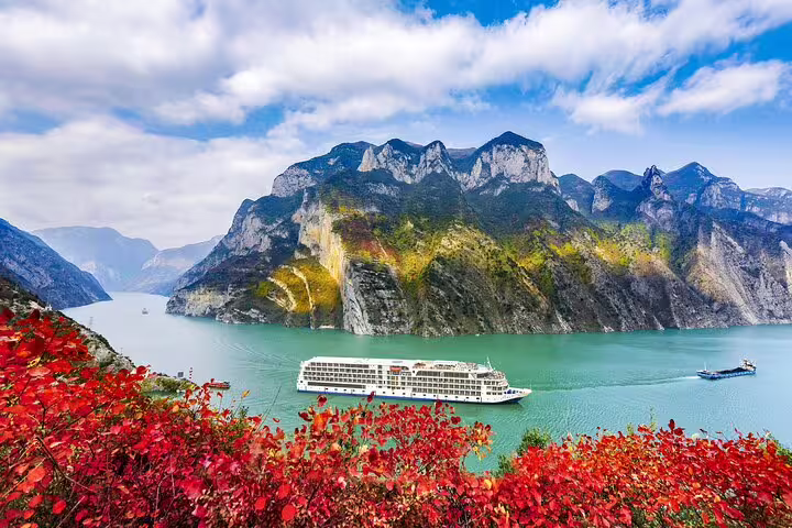Cruise ship sails through the stunning Yangtze River with lush mountains and vibrant foliage in the foreground.