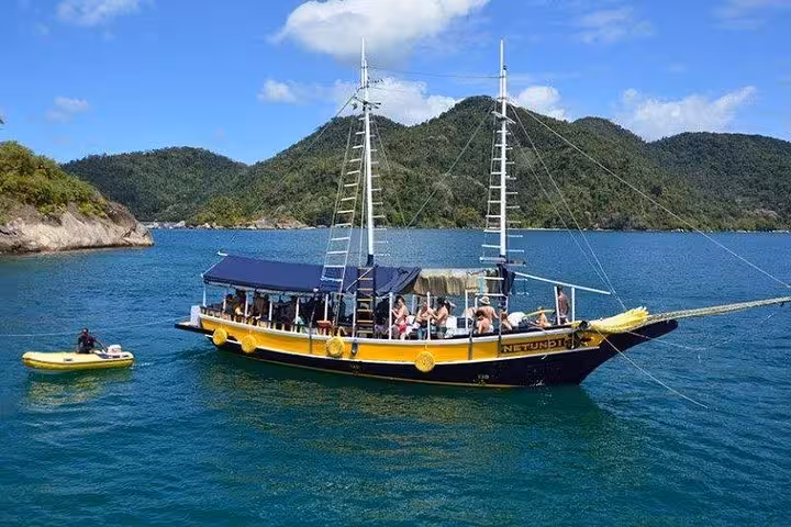Tourists enjoy a scenic boat tour on a yellow vessel named Neptune, set against lush green hills and clear blue waters.