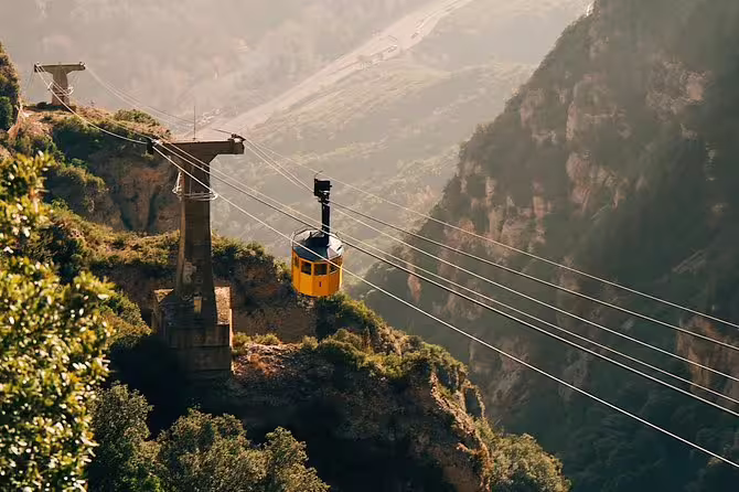 Yellow cable car ascending Montserrat mountain, offering breathtaking panoramic views of the rugged landscape.