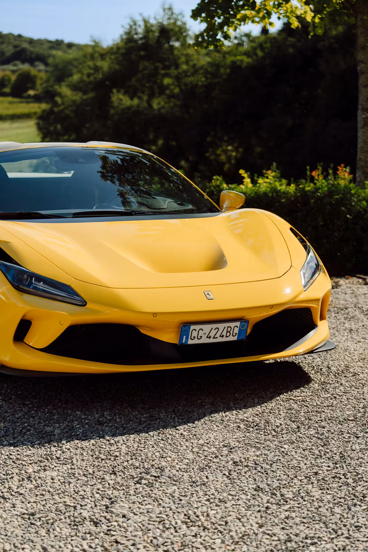 Yellow Ferrari F8 Tributo supercar parked on gravel driveway surrounded by lush Tuscan greenery