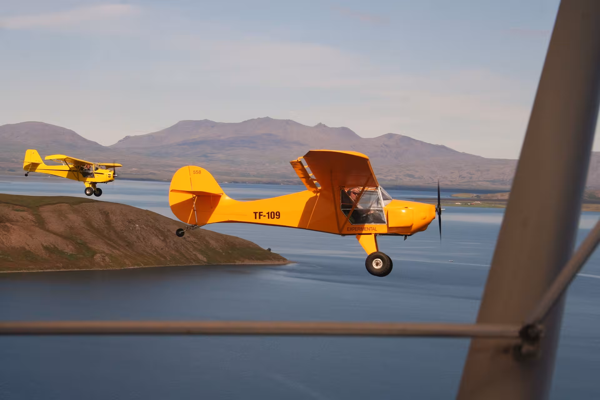 Yellow Flying Buggy light aircraft flying over Iceland fjord and mountains, scenic aerial tour with panoramic views