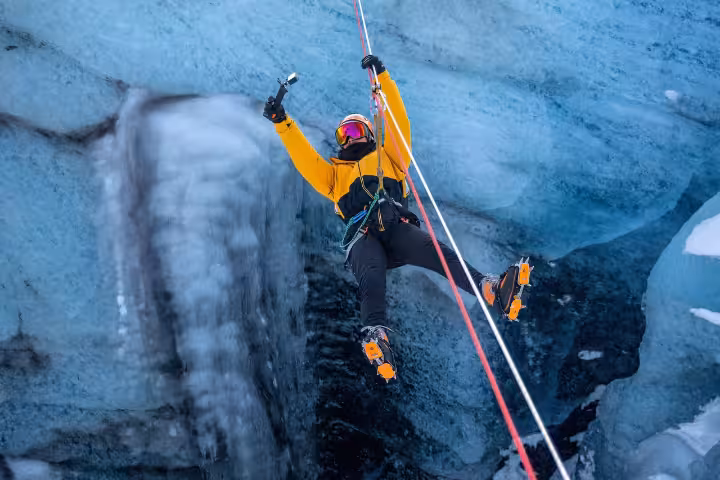 Thrill-seeker in yellow gear zip lining through icy blue glacier walls on a guided Iceland winter adventure