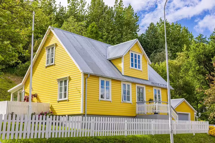 Bright yellow wooden house with white picket fence and silver roof in Akureyri, Iceland