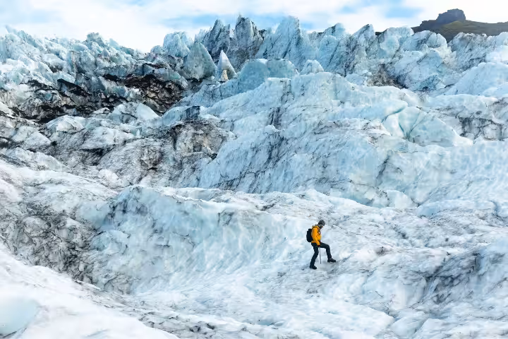 A hiker in a yellow jacket navigating vast blue glacial terrain with ice axe during an extended 5-hour glacier hike.