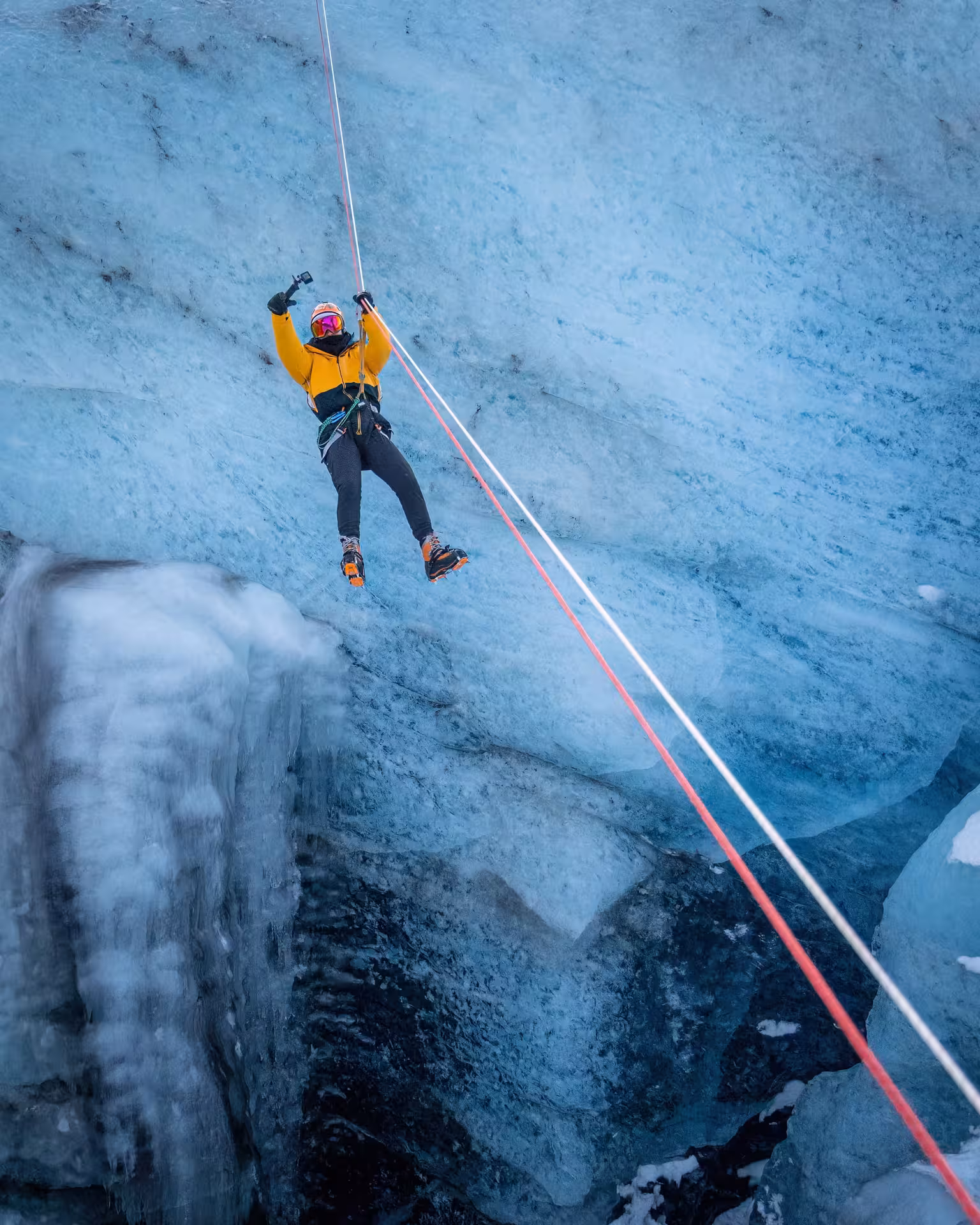 Thrill-seeker in yellow jacket zip lining above deep glacial crevasse on guided Iceland winter glacier adventure