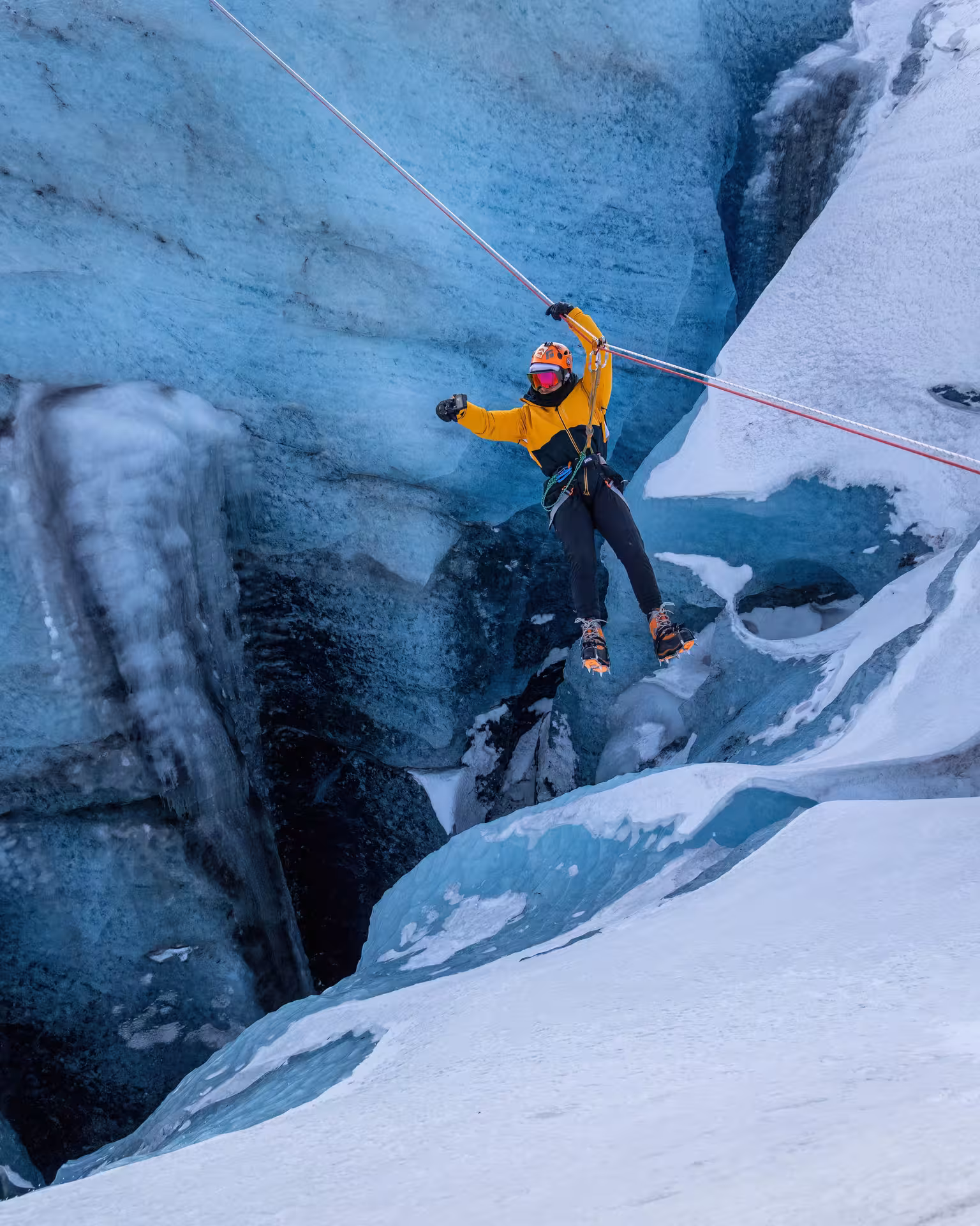 Thrill-seeker in yellow jacket zip lining above a stunning blue ice crevasse on a guided Iceland glacier tour