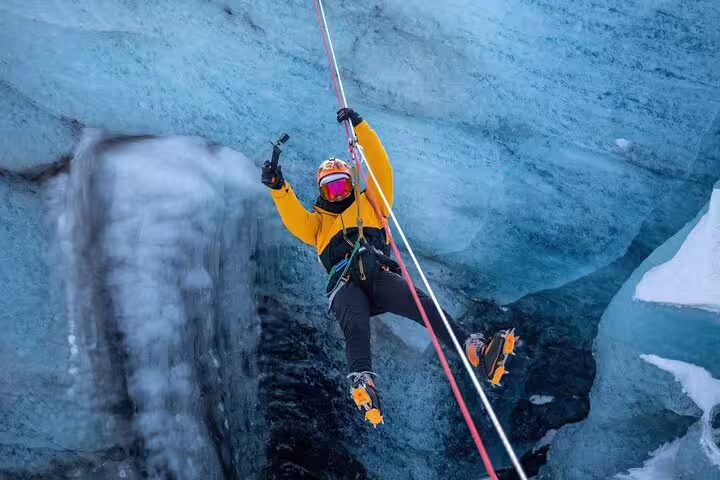 Adventurer in yellow jacket ziplining over glacier crevasse with crampons on exciting Glacier Lagoon adventure tour