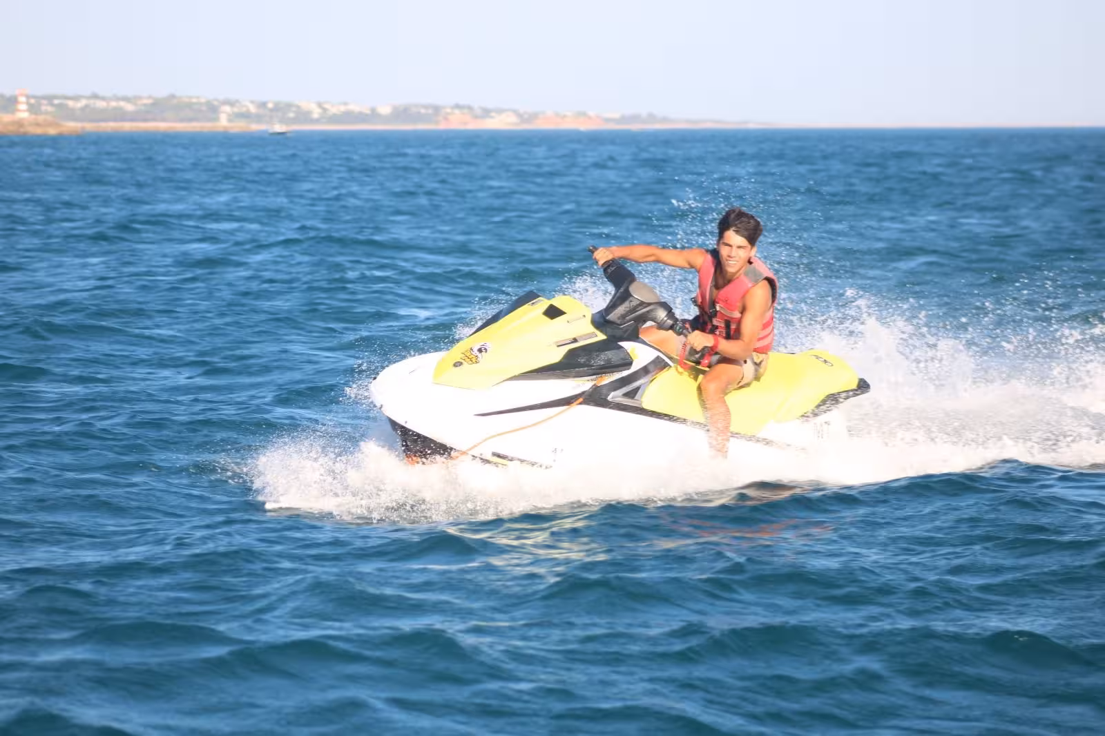 Young man speeding on a yellow jet ski at Praia dos Tomates, enjoying adrenaline-fueled Algarve water sports adventure