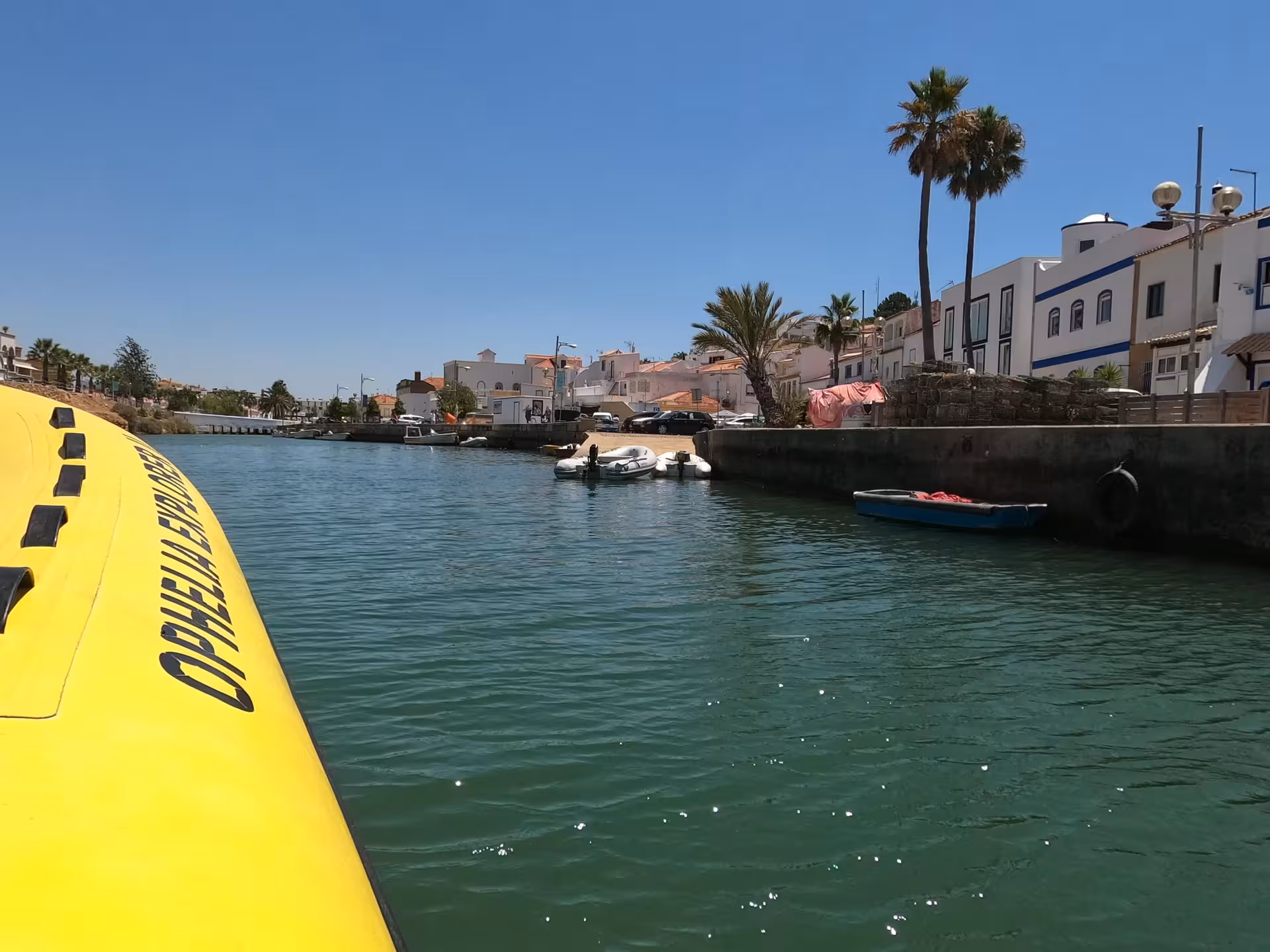 Yellow Super Dia speedboat cruising a sunny Algarve river past whitewashed houses, palm trees and moored fishing boats