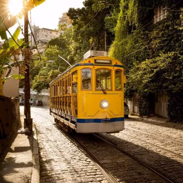 Historic yellow tram navigating the charming cobblestone streets of Santa Teresa under lush green foliage.