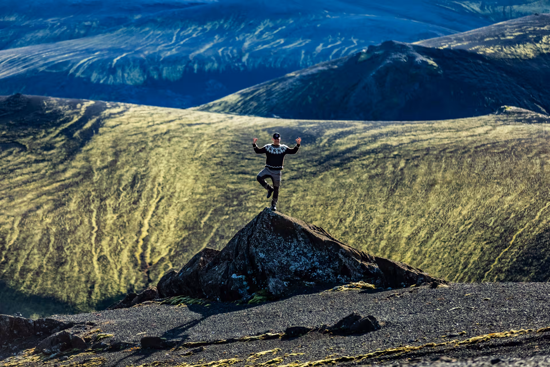 Person balancing on one leg atop a volcanic rock with vast green Icelandic highlands in background