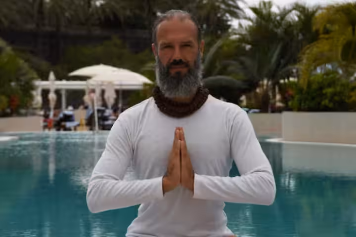 Man in white long-sleeve shirt with prayer hands pose by a pool during yoga retreat
