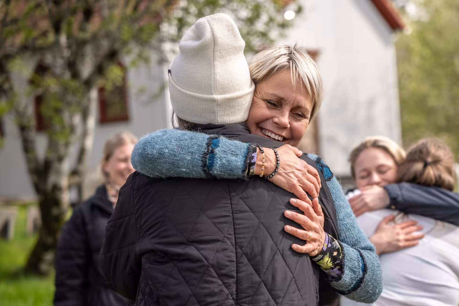 Woman smiling joyfully while hugging another participant during outdoor yoga mindfulness retreat group activity