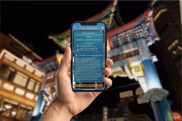 Hand holding smartphone displaying Yokohama Chinatown GPS scavenger hunt app with colorful gate in background