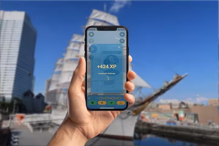 Hand holding smartphone showing +424 XP completed challenge screen on Yokohama walking tour app with tall ship in background